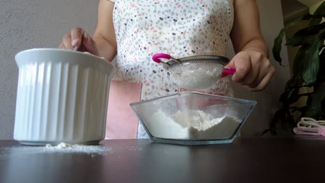 latin woman wearing an apron preparing baking a cake sieving the flour using a metal strainer and a spoon to serve it