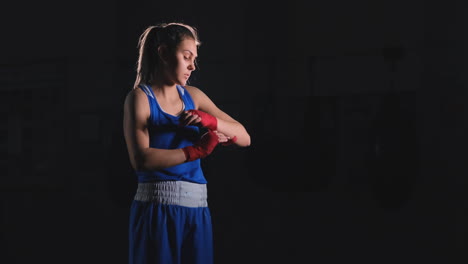 Mittlere-Aufnahme-Einer-Schönen-Athletischen-Boxerin,-Die-Einer-Kämpferin-Rote-Bandagen-An-Den-Händen-Zieht.-Steadicam-Aufnahme