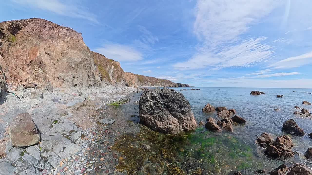 Drone rising on rocky beach to reveal sea cliffs and calm blue sea Ireland Epic Locations in summer
