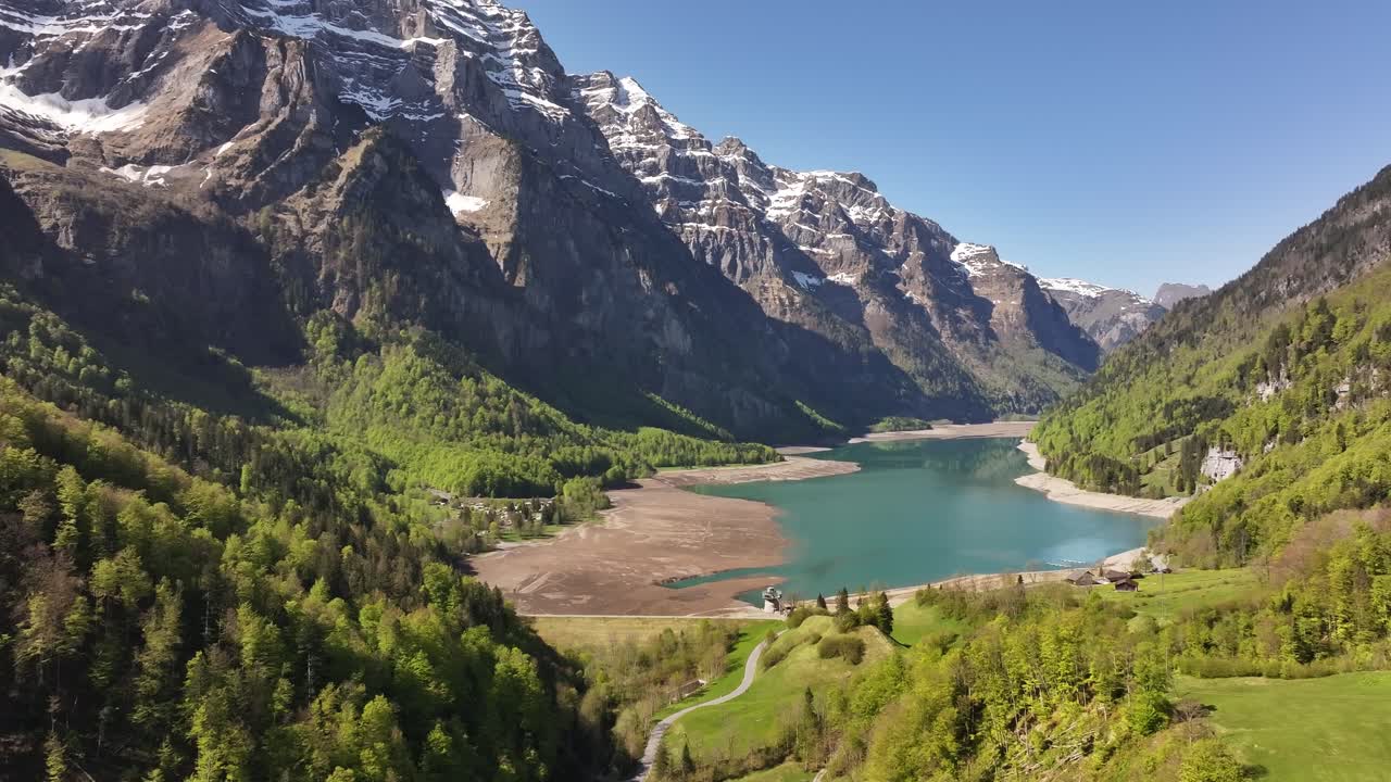 Klöntalersee in Glarus, Switzerland, turquoise lake, green valley and snowy alps under blue sky, beautiful drone pull-back