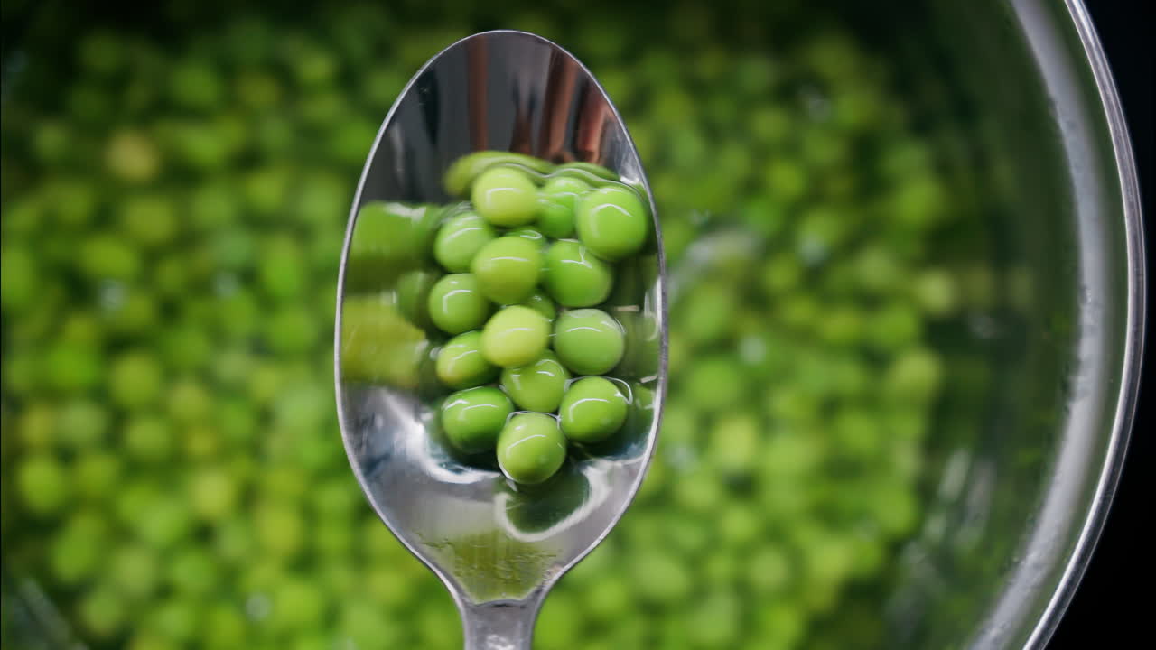 Close up of a spoon picking up green pees with a spoon from a pot with water