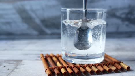 Pouring-white-sugar-in-a-glass-of-water-on-table-,