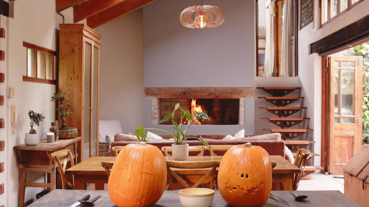 Carved pumpkins on dining table with cozy fireplace in background, at home, Halloween time