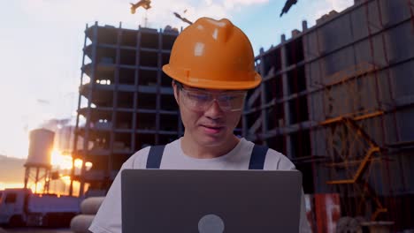 un trabajador asiático señala una computadora portátil en su mano en un sitio de construcción