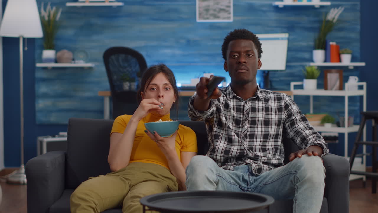 Jovem casal inter-racial assistindo televisão e comendo pipoca