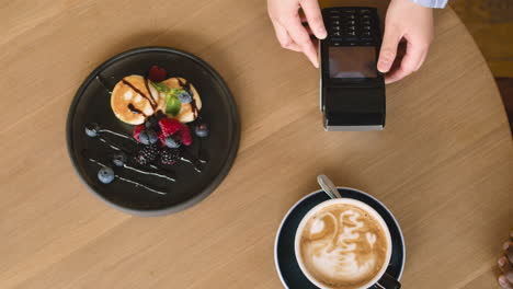 top view of an unrecognizable man paying waiter with contactless credit card in cafe and then drinking cappuccino