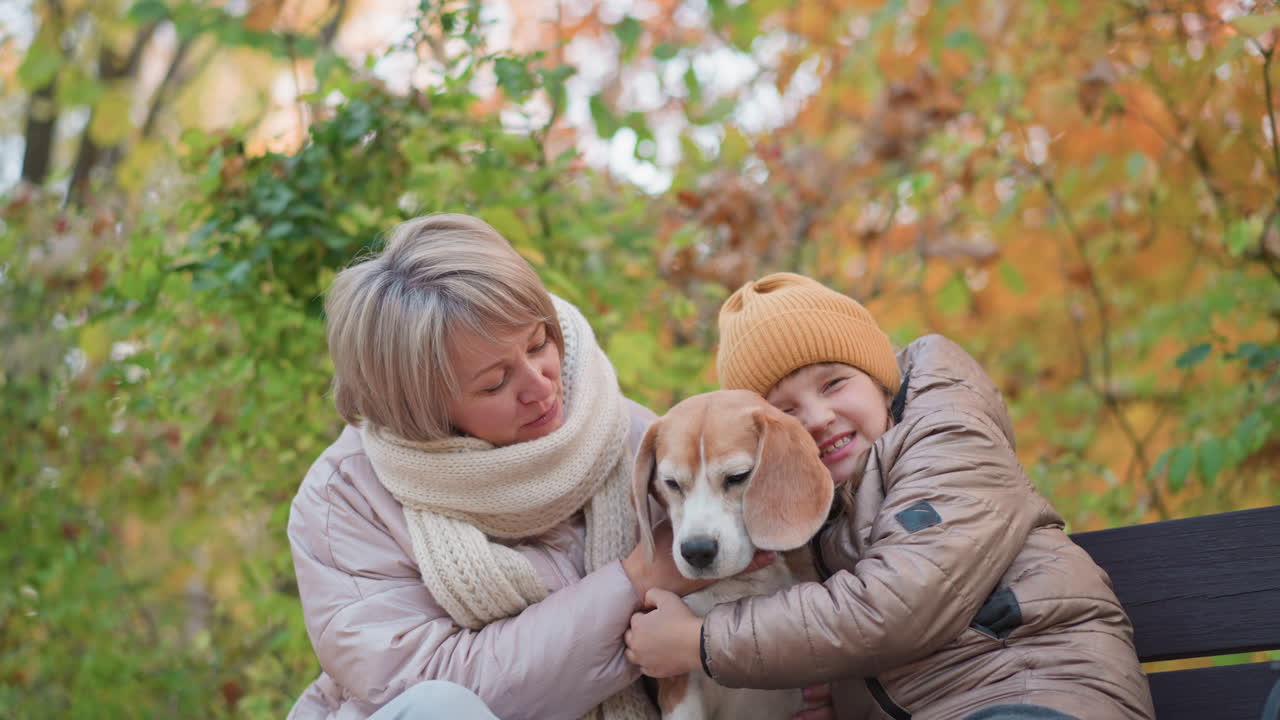 girl holding dog affectionately while mum smiles and looks at dog warmly, cozy autumn setting with soft sunlight, playful expression on child face, tender family moment