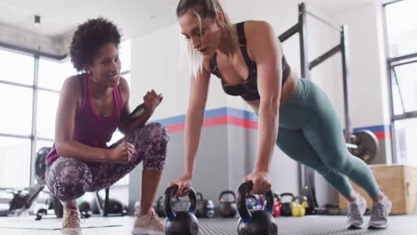 video de una diversa entrenadora de fitness animando a una mujer a hacer flexiones en kettlebells en el gimnasio
