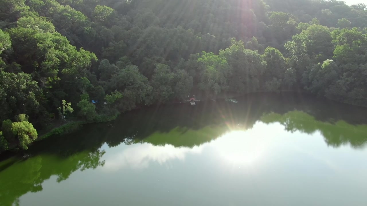 Calm waters of Laguna La María surrounded by dense tropical forest near the base of Volcán de Colima in Colima, Mexico. Backward ascending aerial