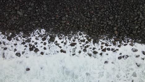 Top-down-static-shot-captures-Hawaii's-Big-Island-rocky-beach-where-moderate-waves-meet-a-pebbly-shoreline