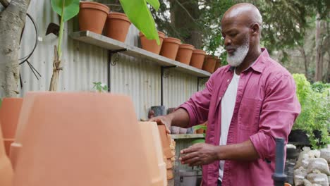Happy-senior-african-american-man-holding-flowerpots-in-garden