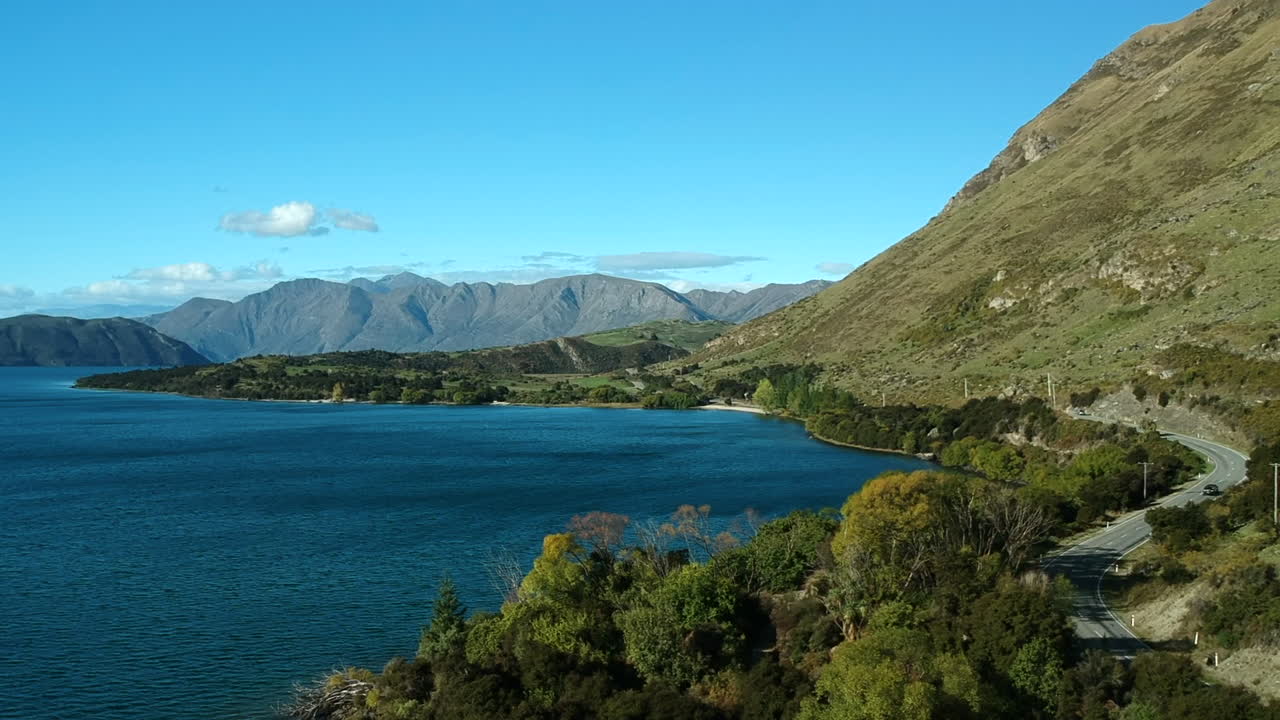 toma aérea del lago wanaka con un coche conduciendo por una carretera en el lado derecho