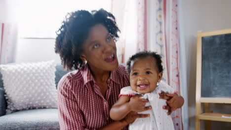 mother lifting baby daughter into the air and smiling at home