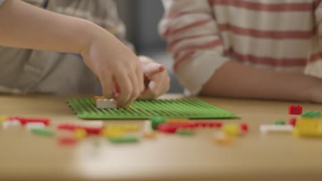 cerca de dos niños jugando con ladrillos de construcción de plástico en la mesa en casa