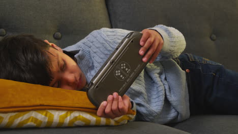 young boy lying on sofa at home playing game or streaming onto handheld gaming device 3