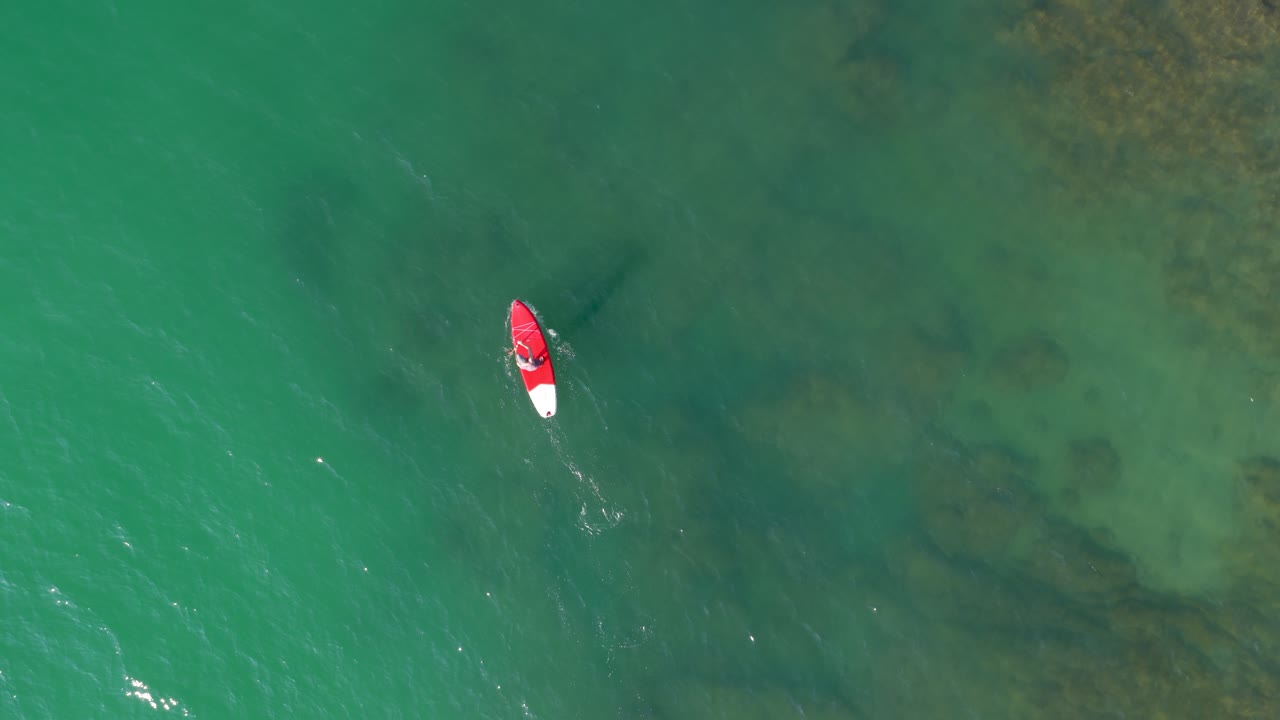 Lifeguard paddling on red paddle board in turquoise water