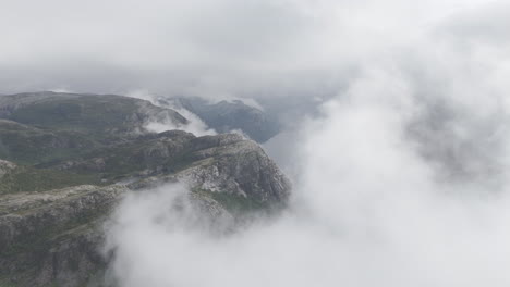 slowmotion drone shot flying through clouds to reveal the water and sea underneath in norway norwegian fjords on a cloudy misty day in between rocky mountains log