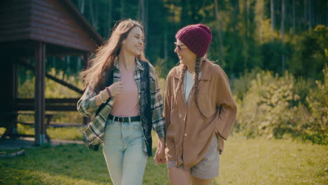 happy female friends holding hands while waking in forest