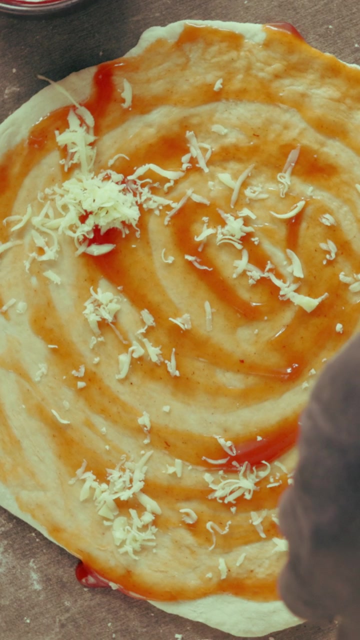 Chef Sprinkling Shredded Cheese onto Pizza Dough with Tomato Sauce