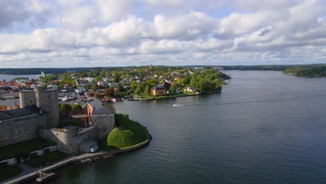 drone shot flying parallel to a boat behind the vaxholm fortress in sweden near stockholm