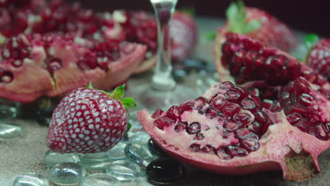 rotating product video of fresh strawberries and pomegranates with beach sand and shiny tones as decoration