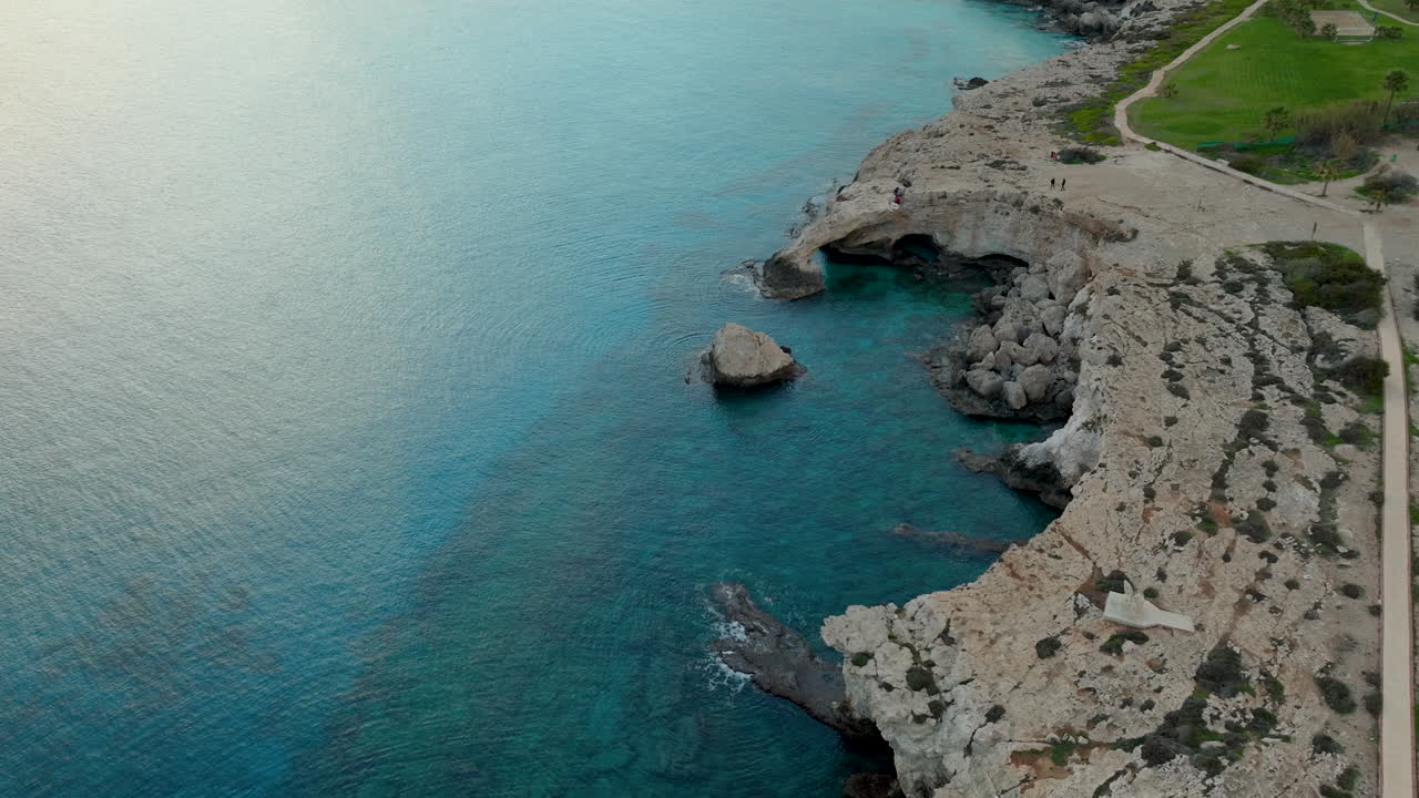 una vista aérea de un arco de roca natural sobre las tranquilas aguas azules del mar mediterráneo cerca de ayia napa, con una costa escarpada y una zona de hierba que conduce al arco