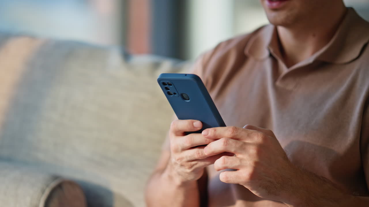 Primo piano di mani di un uomo che tiene un cellulare su un comodo divano durante un fine settimana a casa