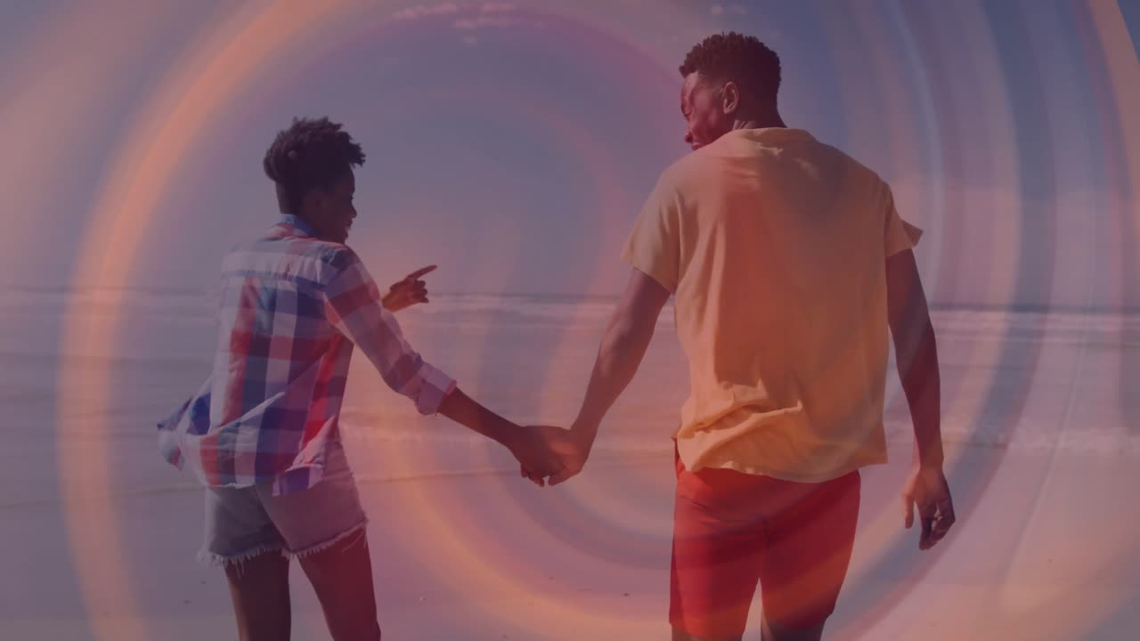 Couple walking hand in hand along shoreline and initiating swirling overlay for travel marketing