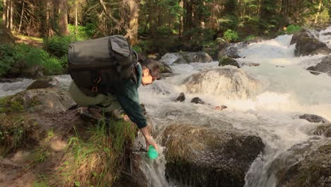 female traveler with a backpack, drinking water in nature in the forest near a mountain river.