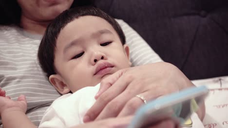 asian baby using smartphones with mom on the bed