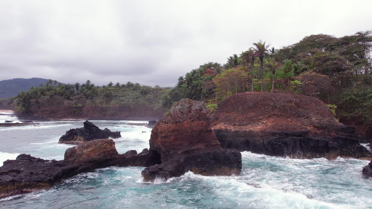 Stormy waves crash on Praia Piscina, São Tomé, a dramatic blend of wild ocean power and serene tropical beach landscape