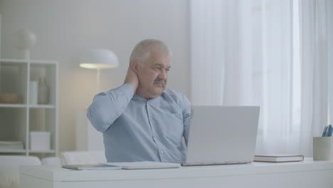 hombre de edad está sintiendo sobreextensión y fatiga del cuello durante el trabajo con el portátil frotando los músculos para relajarse