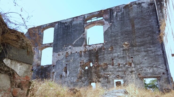 Vista en ángulo bajo de los muros de piedra desmoronados y los marcos de ventanas vacíos de las históricas ruinas de la Hacienda Coahuixtla bajo un cielo azul claro.