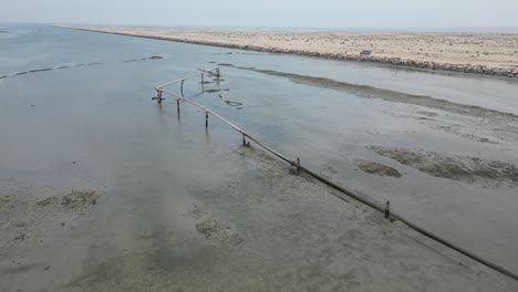 River-with-low-water-level-next-to-desert-terrain,-irrigation-pipes