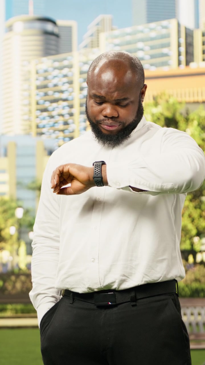 Vertical Video Worried businessman looking down at smartwatch while standing outdoors