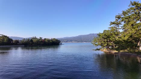 pine trees reflecting on the calm blue waters of miyazu bay in autumn, with amanohashidate sandbar in the background