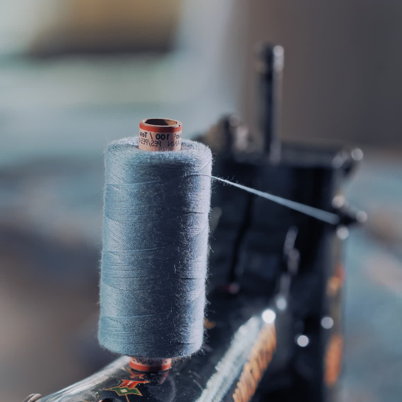 Close-up of a bobbin of blue thread on the sewing machine spinning. Cotton reel spinning on sewing machine for making dress in atelier. Slow motion.