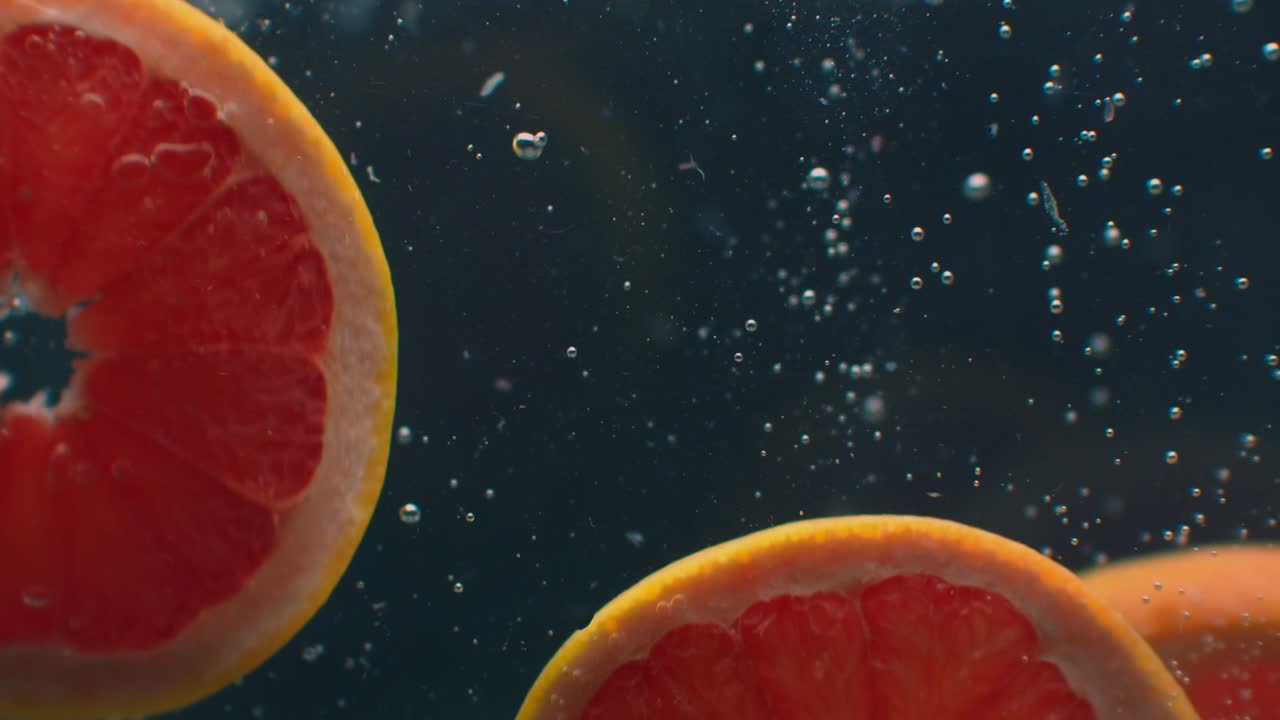 3 fette di pompelmo sott'acqua con bolle d'aria e al rallentatore. Fresco, succoso, sano e vegetariano