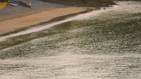 sunrise view along beach with sand shoreline and boats moored on pebbles