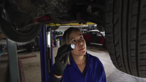 Female-mechanic-using-a-torch-light-and-working-under-a-car-at-a-car-service-station