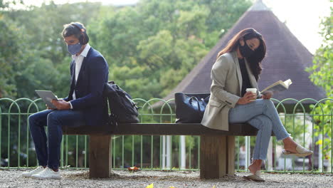 hombre de negocios y mujer de negocios con máscaras en un descanso leyendo un libro y viendo una tableta digital