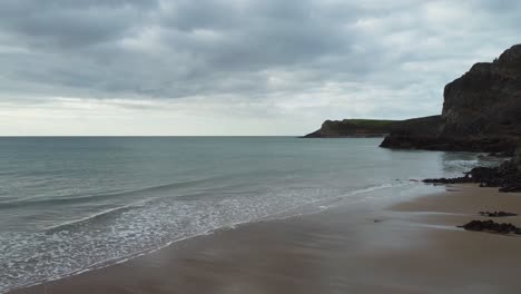 Wales-Mewslade-Bay-Luftaufnahme-Zum-Meer-Mit-Felsigen-Klippen-Und-In-Der-Ferne-Sichtbarer-Küste-Mit-Dramatisch-Bewölktem-Himmel-4k