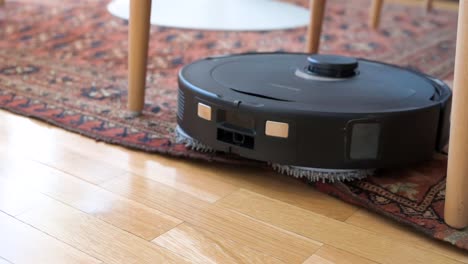 imágenes en cámara lenta de un robot aspirador autónomo que pasa de un piso de madera a una alfombra en una sala de estar