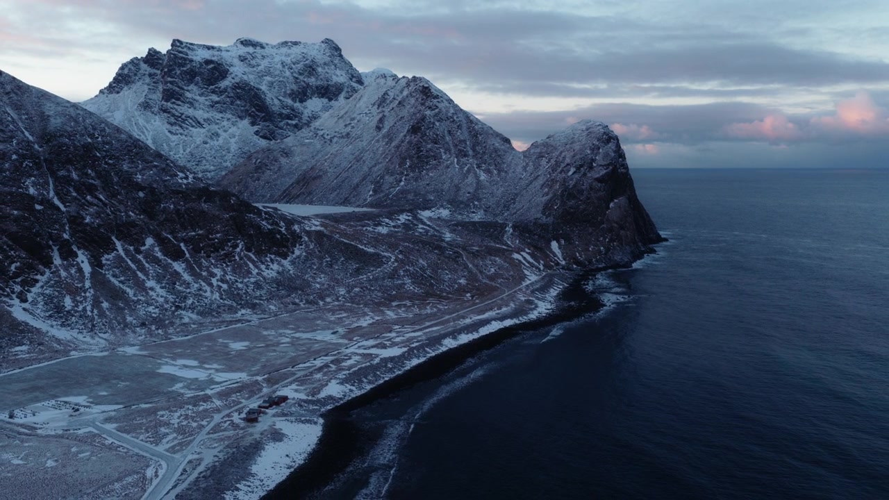 Raue arktische Küstenlinie mit schneebedeckten Bergen über ruhigem Meer, Drohne etabliert Hintergrund, Rückwärtsfahrt.