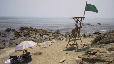 life guard sits on duty in her post on the beach near cala de mijas on the costa del sol in southern spain as a holiday makers sits beneath parasol looking at mobile pone.