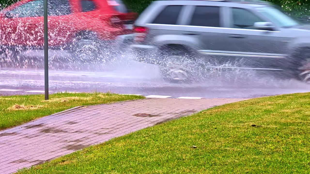 Cars Driving Through Large Puddle Splashing Water After Heavy Rain on City Street