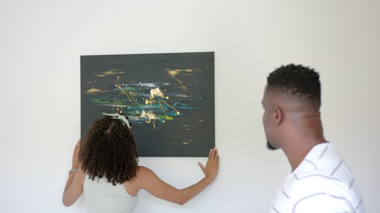 Admiring abstract painting, couple discussing artwork in modern home living room