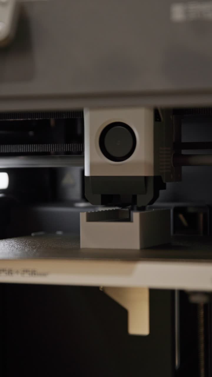 A vertical, close-up shot of a 3D printer extruder head actively depositing filament to build a precise plastic component layer by layer