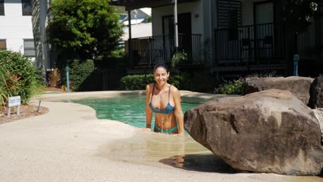 Wunderschöne-Frau-Taucht-In-Den-Pool-Ein-Und-Kommt-An-Einem-Heißen-Sommertag-Mit-Wasser-Heraus,-Das-Von-Ihrem-Körper-Tropft