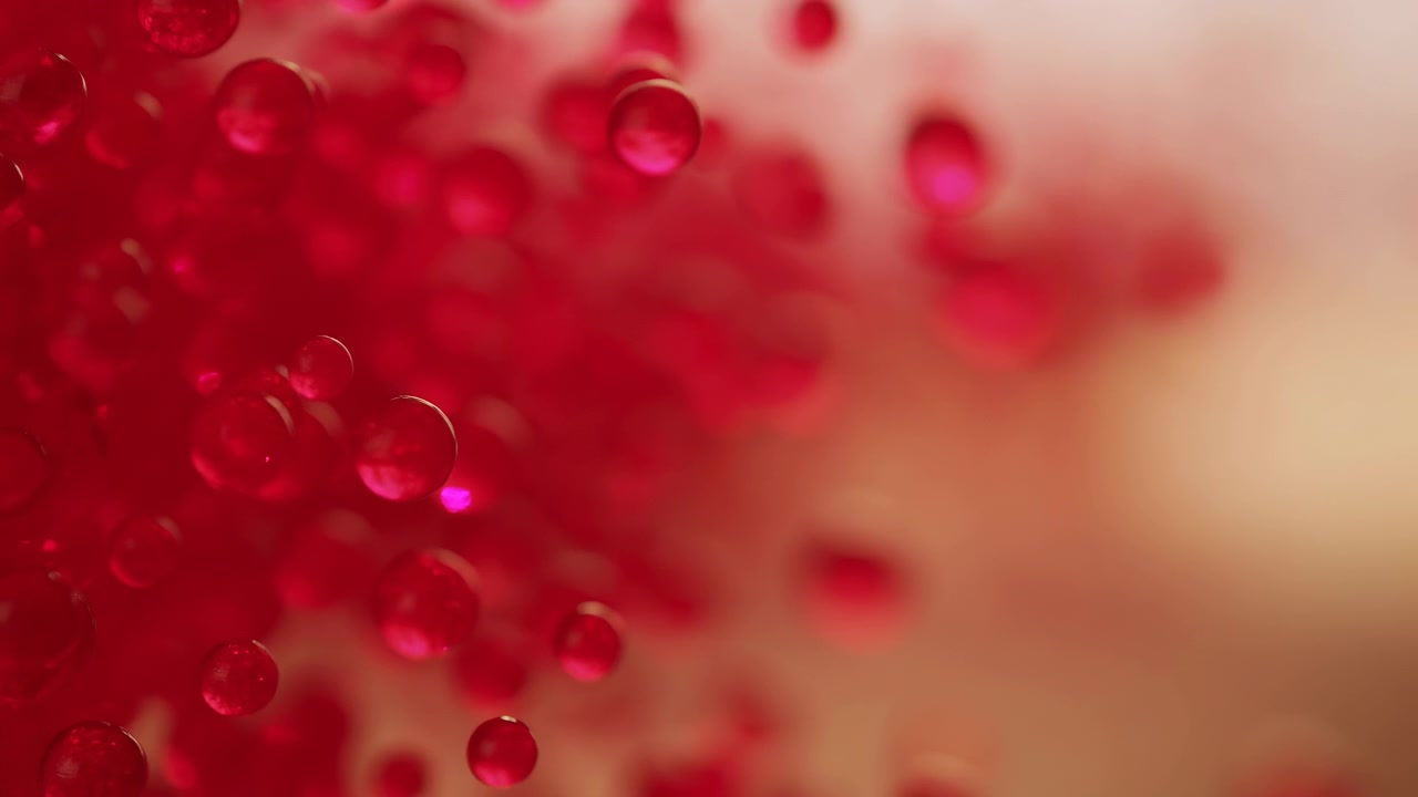 Dense cluster of translucent red gel beads sits on left side while individual beads separate, float, and soften into blur across warm gradient background, creating glossy highlights, layered depth